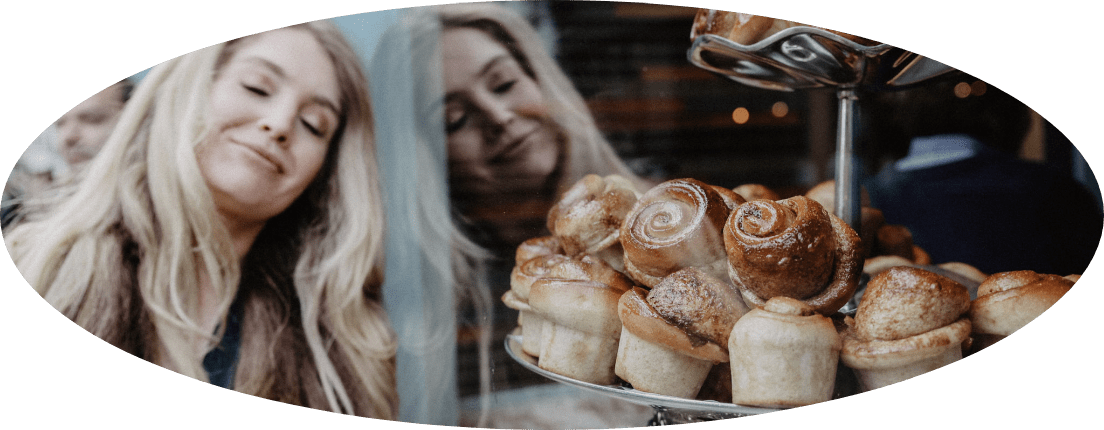 Katie is leaning on the window of a bakery shop.